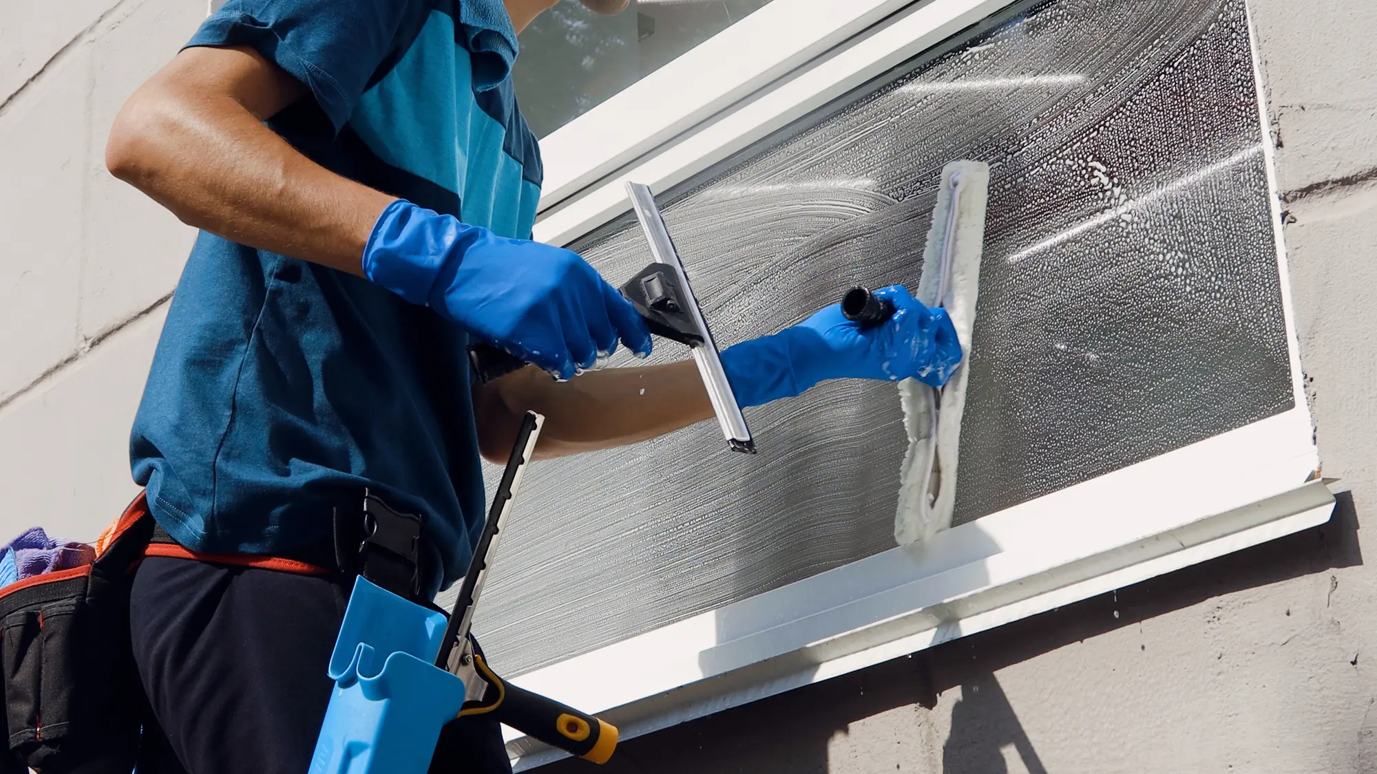 Eine Person mit blauen Handschuhen putzt konzentriert ein Fenster mit weißem Rahmen